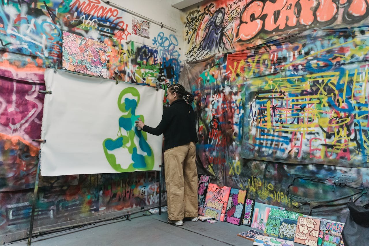 Graffiti artist in studio painting vibrant mural on canvas surrounded by street art.